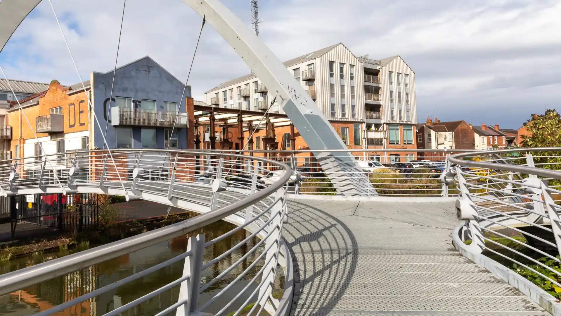 A curved pedestrian bridge with metal railings leading towards a modern residential and office area
