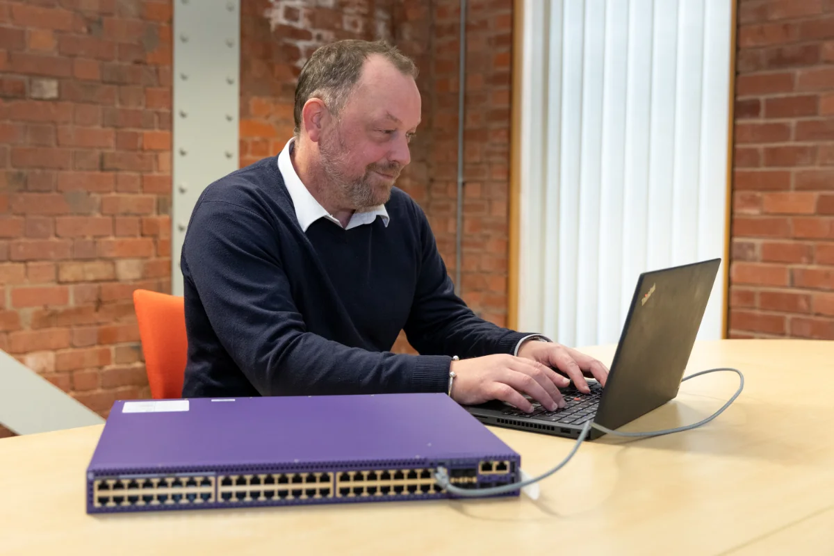 Man working on a laptop at a round table in a modern office with exposed brick walls