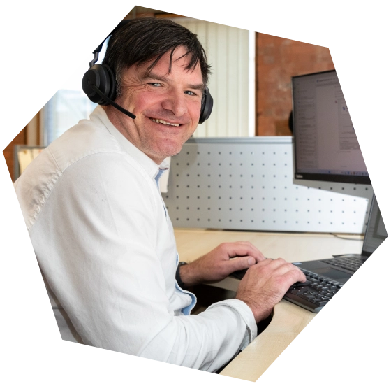 Man wearing a headset and white shirt smiling while working on a laptop