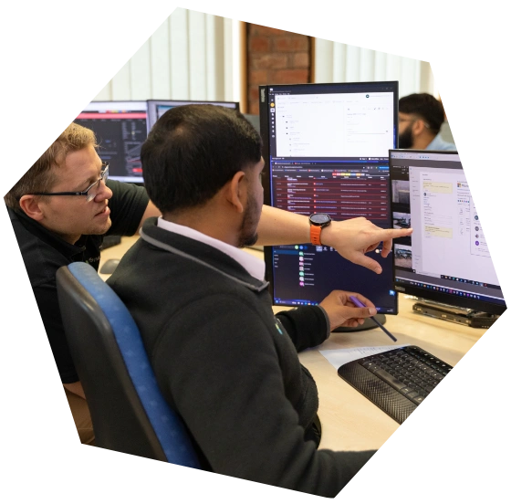 Two colleagues collaborating at a desk with multiple monitors