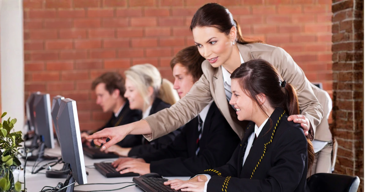 Teacher supporting students working at computers in a school IT suite