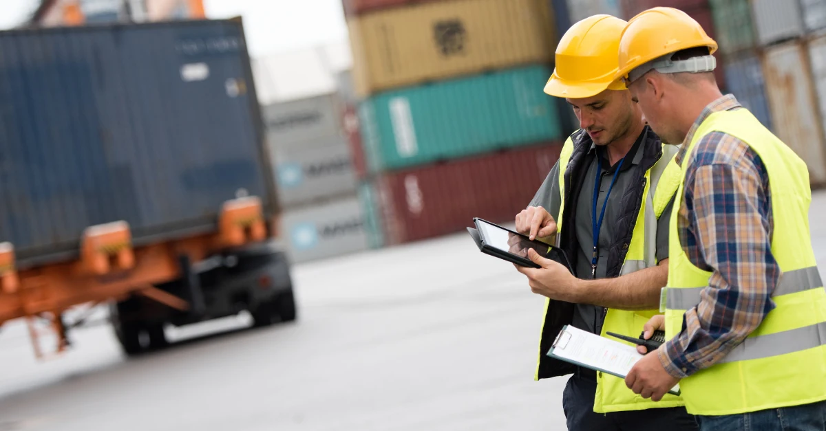Two workers checking data on a tablet at a logistics yard