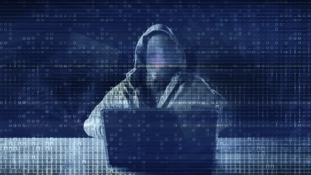 Hooded figure at a laptop with a faint face, overlaid by glitching binary code in a dark blue digital scene.
